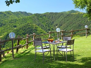 Ein Tisch mit Stühlen und einer Tischlampe auf einem grasbewachsenen Hügel mit einem Holenzaun und einem schönen Blick auf einen bewaldeten Berg.