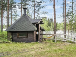 A small wooden cabin with a hexagonal roof, a chimney, and a door leading to a porch.