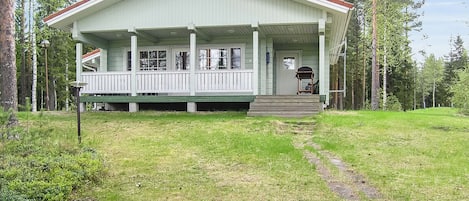 Une maison à deux étages avec un porche, entourée d’une pelouse et de grands arbres.