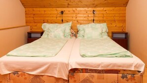 A room with a sloped wooden ceiling, two beds with matching bedding, and two bedside tables. - Vacation home Gerle by Interhome (Balatonfenyves)