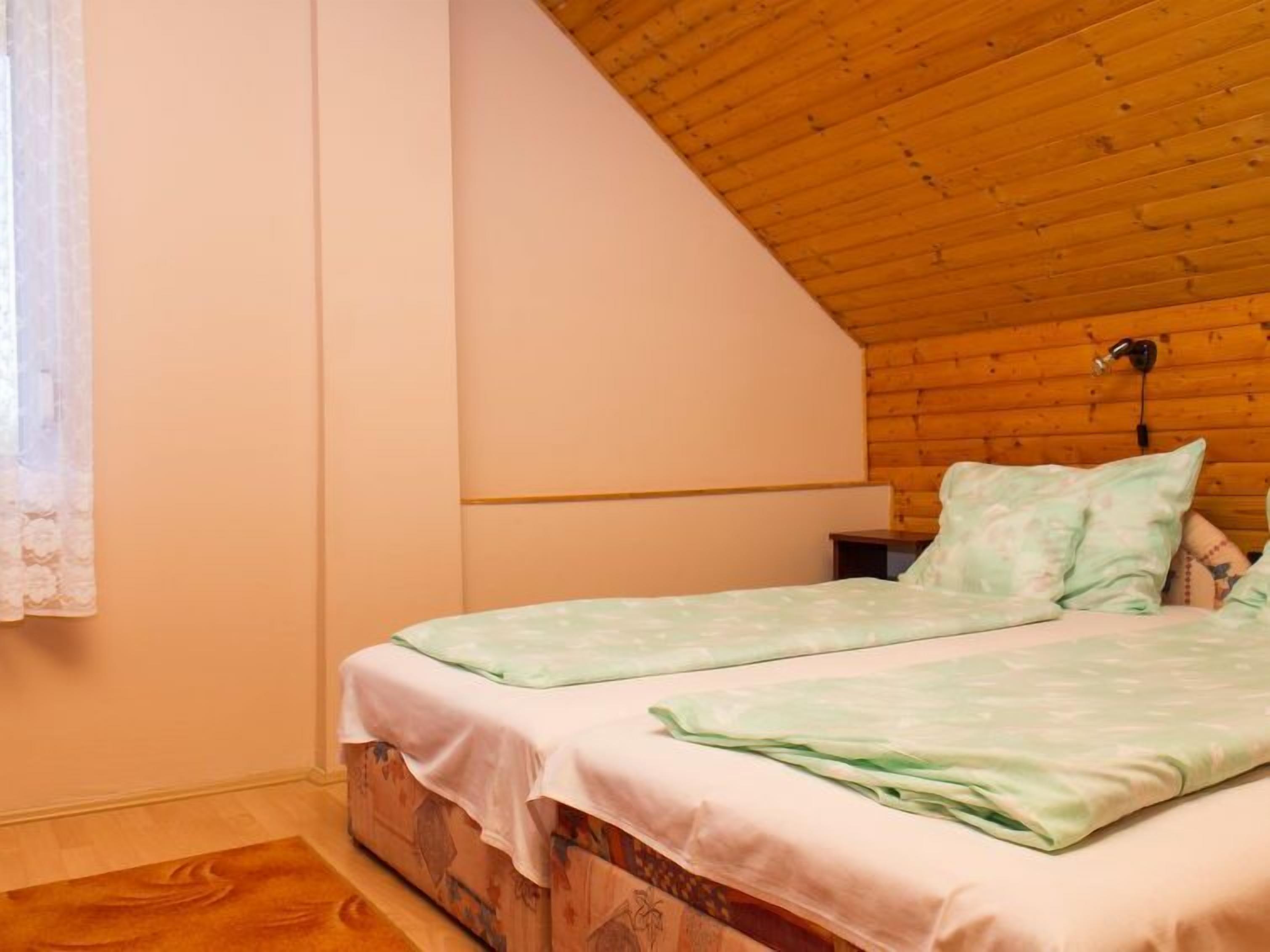 Un dormitorio con dos camas, techo de madera y ventana con cortinas de encaje.