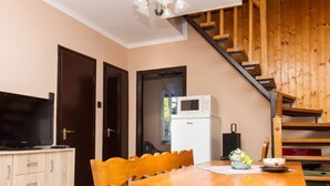 A cozy kitchen with a wooden table, chairs, a microwave, and a television on a cabinet. - Vacation home Gerle by Interhome (Balatonfenyves)