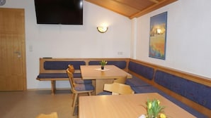 Ett rum med ett träbord och en bänk som sittplats, en platt-TV som hänger på väggen och en tavla på väggen.