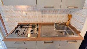 Una cocina con estufa a gas, pileta y salpicadero de azulejos.