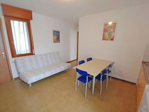 A small room with a sofa, a table, and chairs. There are two paintings on the walls.