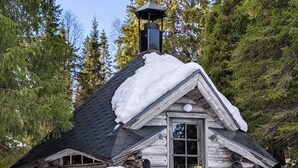 En timmerstuga med ett snötäckt tak, en skorsten och ett fönster.