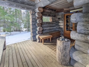 Una cabaña de troncos con una terraza de madera, un banco y una chimenea de piedra.