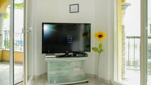 A living room with a flat-screen TV on a glass cabinet, a sunflower vase, and a balcony door. - Residenza Moro by Interhome (Ascona)