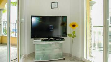 Ein Wohnzimmer mit einem Flachbildfernseher auf einer Glasschranke, einer Sonnenblumenvase und einer Balkontür.