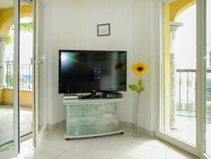 A living room with a flat-screen TV on a glass cabinet, a sunflower vase, and a balcony door. - Residenza Moro by Interhome (Ascona)