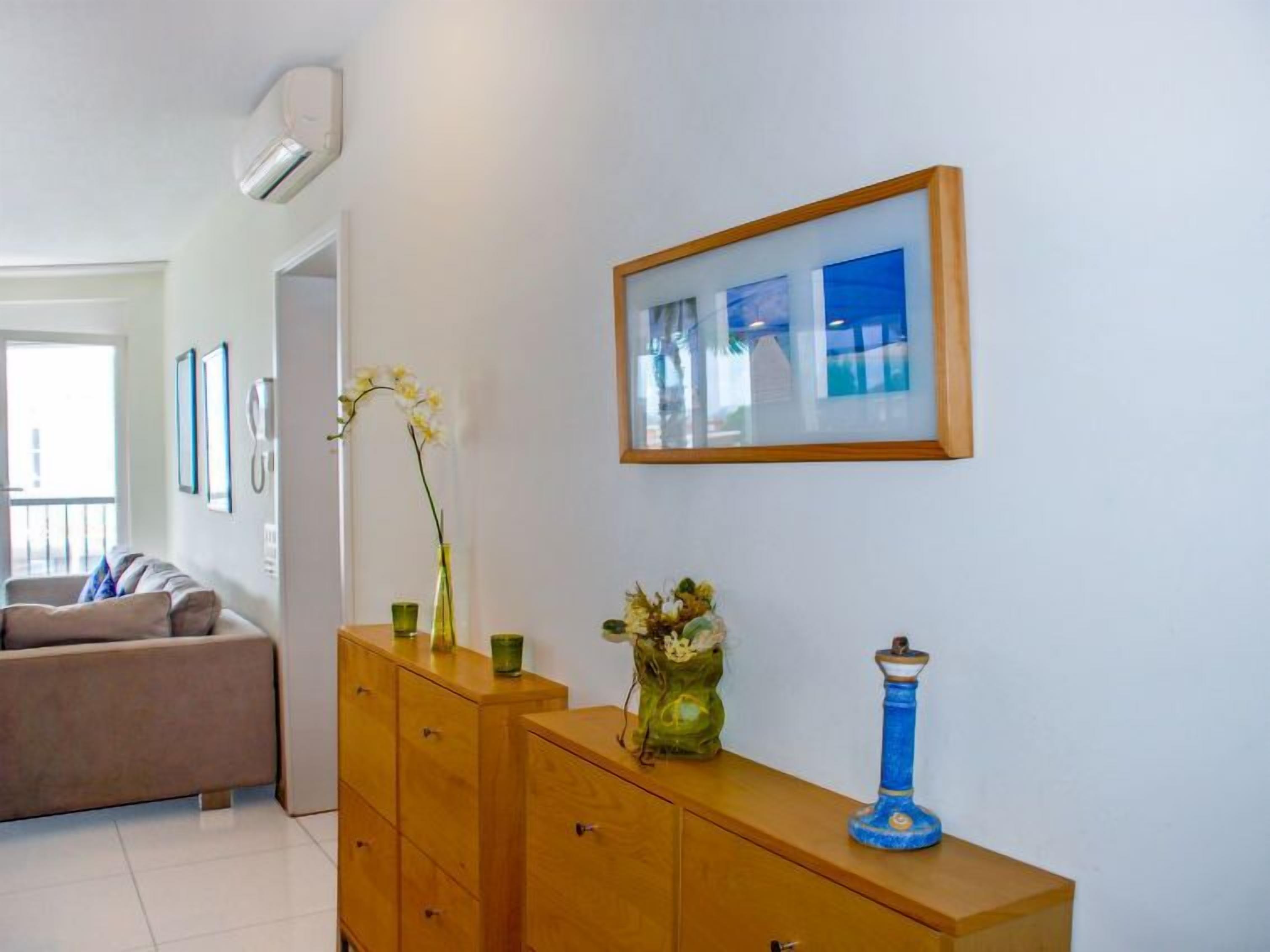 Ein Wohnzimmer mit einem Holzschrank, einer Vase mit Blumen und einem gerahmten Bild an der Wand.