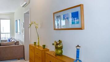 Ein Wohnzimmer mit einem Holzschrank, einer Vase mit Blumen und einem gerahmten Bild an der Wand.