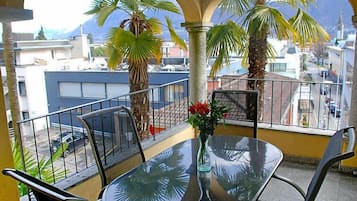 Ein Balkon mit Glastisch und Stühlen, umgeben von Palmen und Blick auf Gebäude.