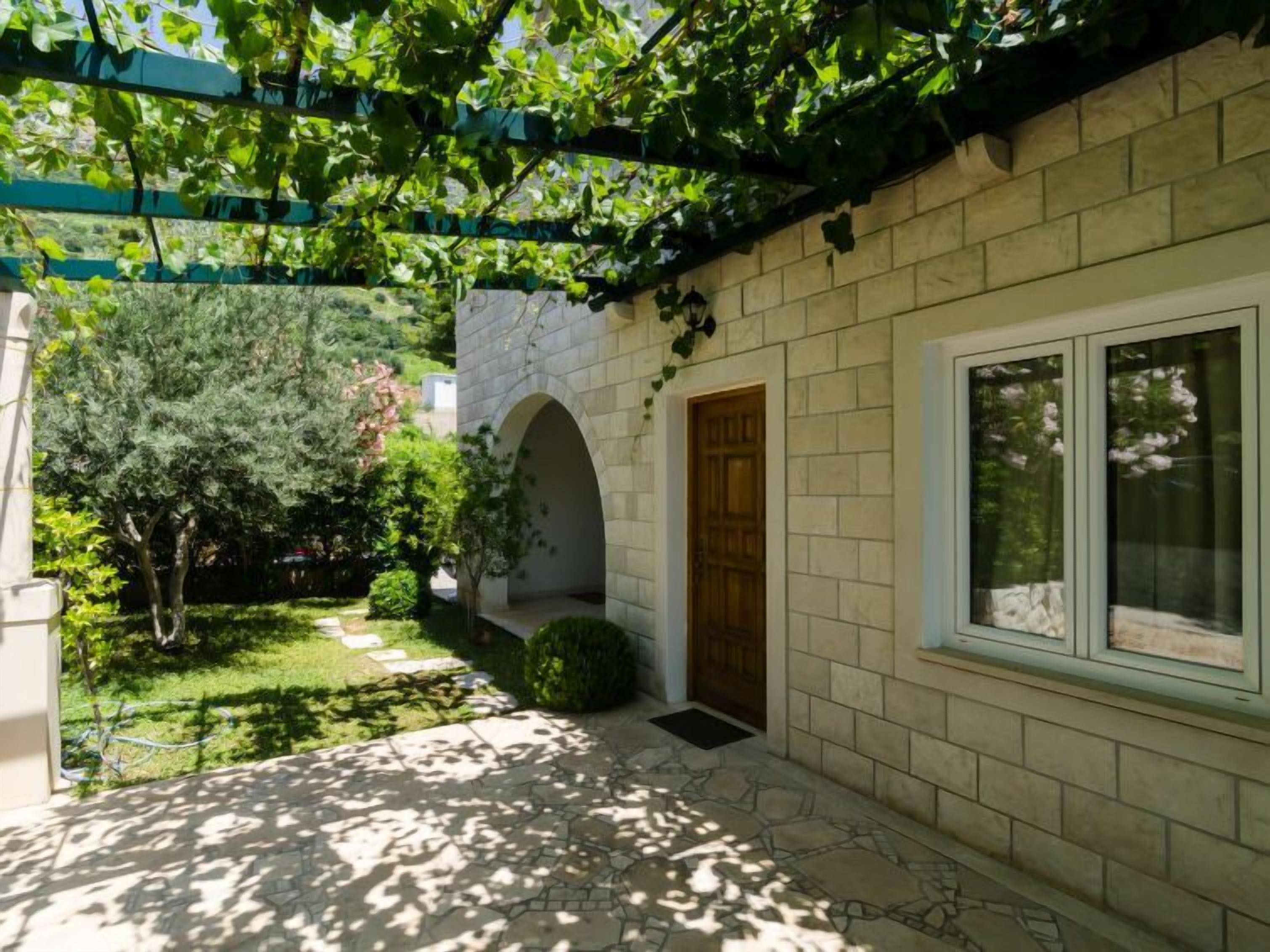 A courtyard with a stone pathway, a wooden door, and a window overlooking a garden.