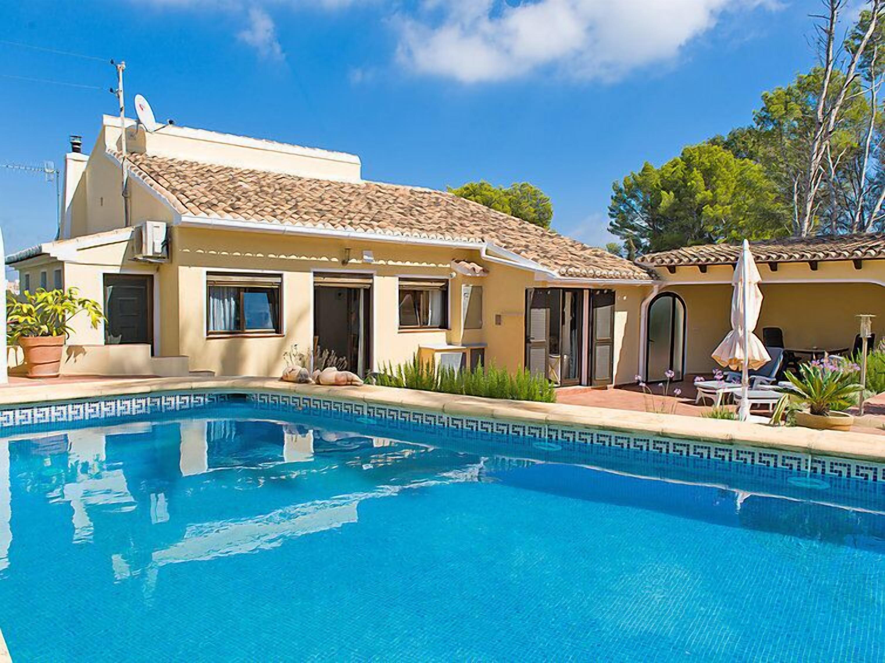 Uma casa de dois andares com piscina, um pátio com mobiliário de exterior e uma antena parabólica.