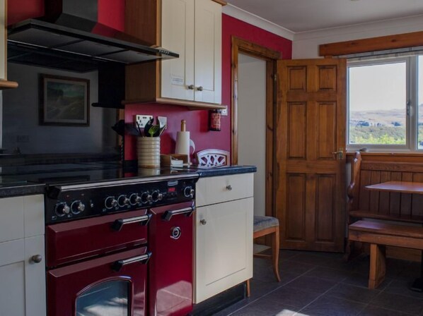 A kitchen with a red stove, white cabinets, and a wooden door. - Viewfield by Interhome (Isle of Skye)
