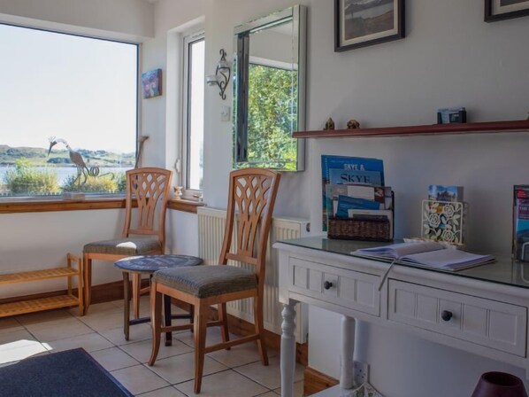 A room with two wooden chairs, a small round table, a white dresser, and a window with a view of greenery and a bird sculpture. - Viewfield by Interhome (Isle of Skye)