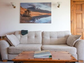 A beige sofa with a plaid throw blanket, a wooden coffee table with a magazine, and a landscape painting above. - Viewfield by Interhome (Isle of Skye)