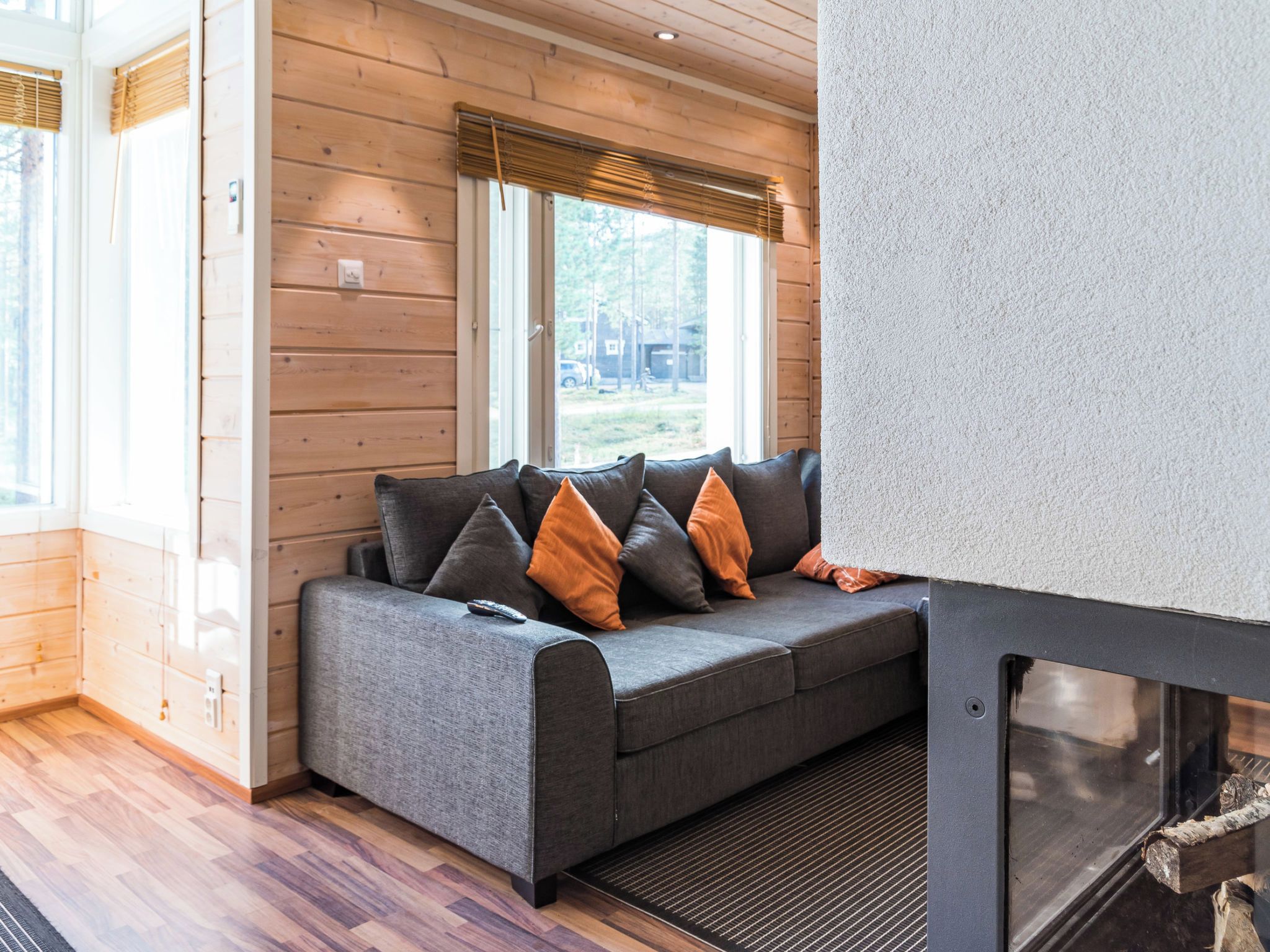 A cozy seating area with a sofa and cushions, wooden walls, and a window with blinds.