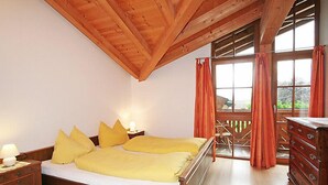 A bedroom with a wooden ceiling, a bed with yellow bedding, a nightstand with a lamp, a dresser, and a window with curtains.