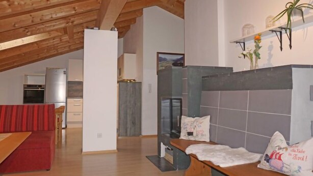 A spacious living area with a high ceiling, wooden beams, a red sofa, a bench, and a tiled fireplace wall.