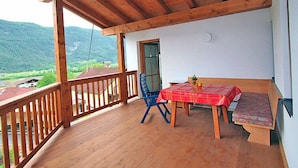 A wooden balcony with a table and chairs, a view of the mountains, and a door to the room.