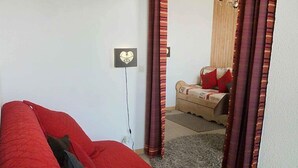 Una habitación con un sofá rojo, una cama pequeña con ropa de cama estampada, una lámpara fijada a la pared y una alfombra.