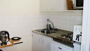 Una cocina compacta con armarios blancos, un lavamanos de acero inoxidable, un hervidor, una estufa y un microondas.