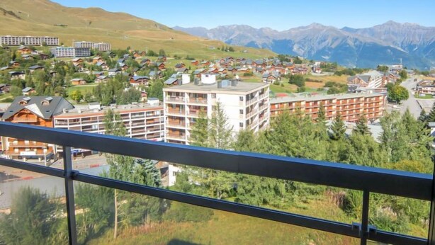 Un complejo turístico de montaña con varios edificios, incluyendo un edificio blanco destacado con balcones, rodeado de vegetación exuberante y montañas al fondo.