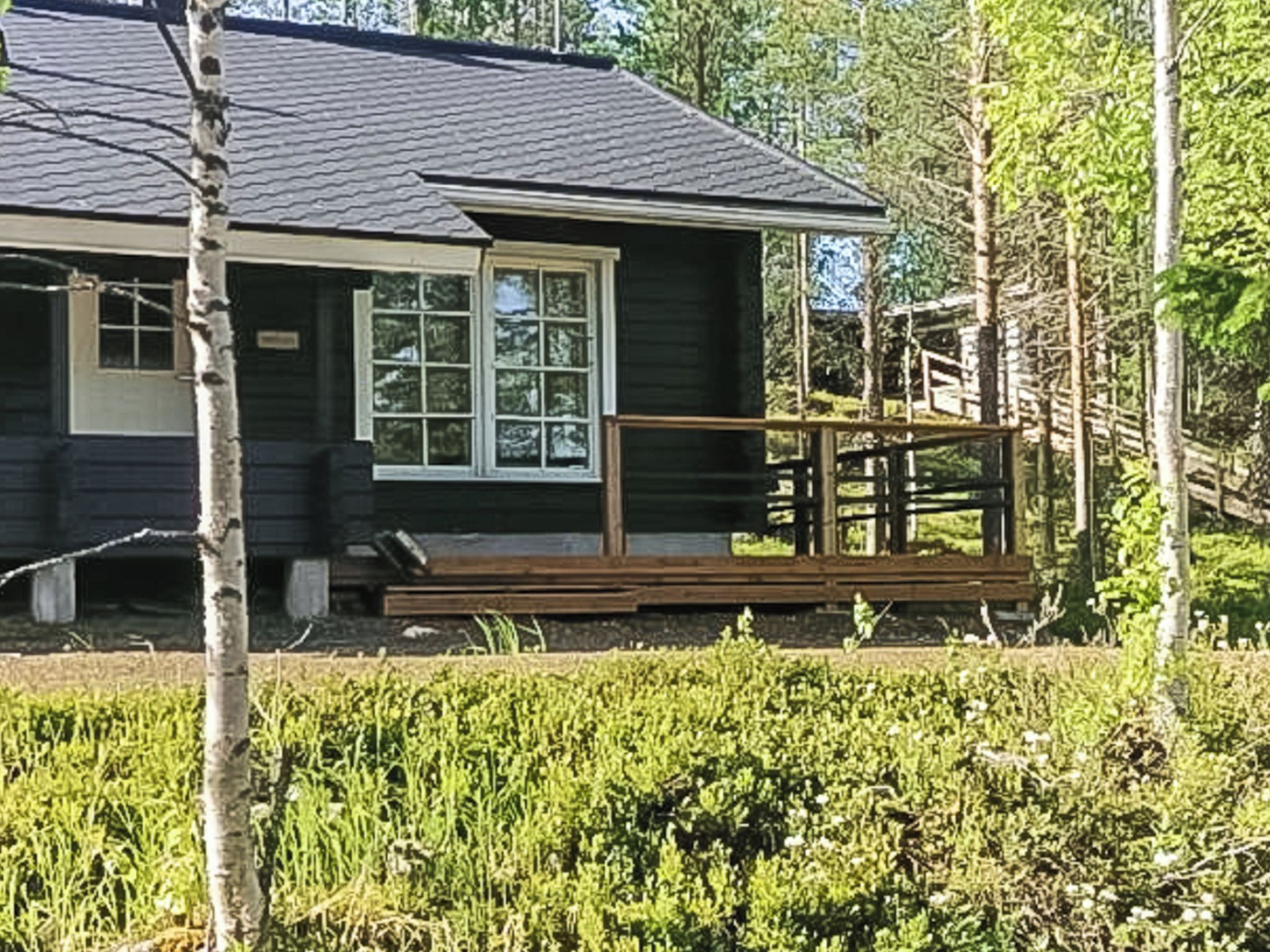 Mökki, jossa on kuisti, ja jonka ympärillä on puita ja kasvillisuutta.