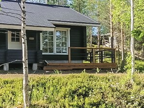 Une cabane dotée d’une véranda, entourée d’arbres et de végétation.