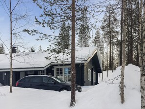 Une cabane devant laquelle est garée une voiture, entourée d’un paysage enneigé et d’arbres.