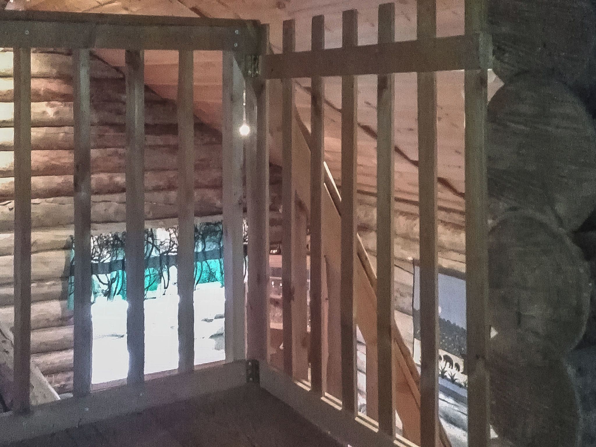 A log cabin interior with a wooden staircase and a view of the outdoors.