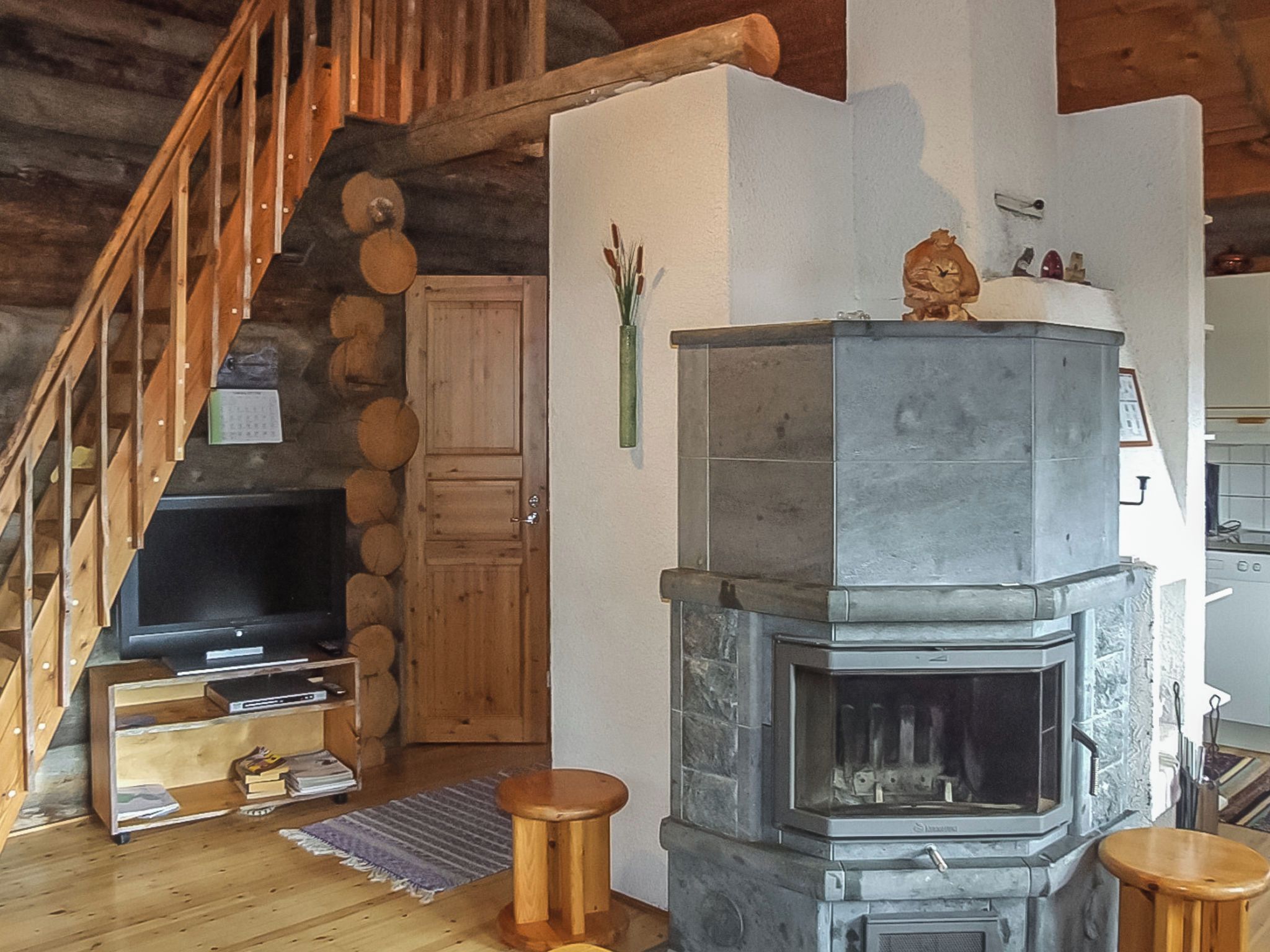 A rustic interior with a stone fireplace, wooden staircase, and a television on a wooden stand.