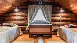 Een gezellig houten blokhut slaapkamer met een centraal bed en twee kleinere bedden aan weerszijden.