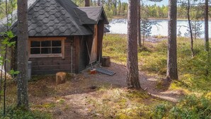 Een klein huisje met een zeshoekig dak, omringd door bomen en een wateroppervlak.