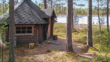 A cabin with a hexagonal roof, surrounded by trees and a lake.