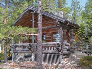 Eine Blockhütte mit einer Holzterrasse, umgeben von Bäumen und einem Kiesweg.