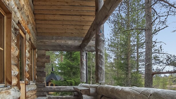 Een houten hut met een veranda, houten banken en uitzicht op een bos.