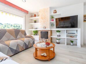 En stue med sofa, pejs, fjernsyn og reoler med planter og pynt.