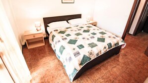 A bedroom with a bed, two bedside tables, a nightstand, a framed picture on the wall, and a tiled floor. - Valbella by Interhome (Bibione)