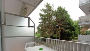 A balcony with a white table and chairs, a small green object on the table, and a view of trees and a building in the background. - Valbella by Interhome (Bibione)