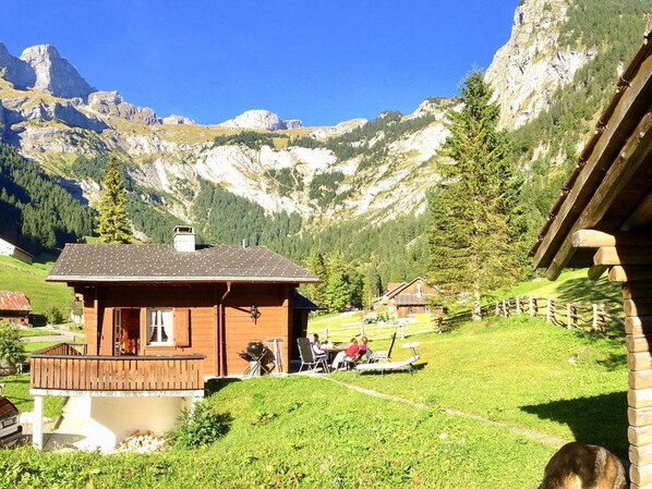 Un chalet de madera con balcón, rodeado de un paisaje verde exuberante y montañas al fondo.