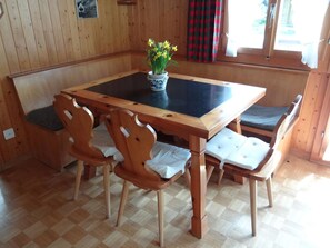 Una mesa de comedor de madera con superficie negra, rodeada de sillas de madera con asientos acolchados.