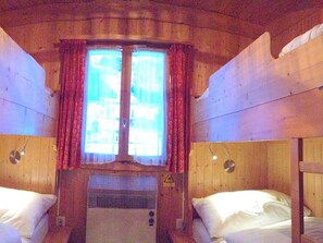 A cabin with two beds, a window with curtains, and a heater. - Chalet Bergmandli Appartement/Fewo 8-Bettwohnung by Interhome (Engelberg)