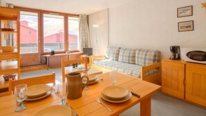 A cozy room with a dining table set for four, a sofa, a television, and a kitchenette. - Grandes Platières II by Interhome (Tignes)