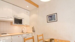 A compact kitchen with white cabinetry, a built-in oven, and a dining area with a wooden table set for two. - Grandes Platières II by Interhome (Tignes)