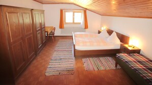 A bedroom with wooden ceiling beams, a large bed with a checkered bedspread, a bedside table with a lamp, and a window with curtains. - Jägerhof by Interhome (Schwaz)