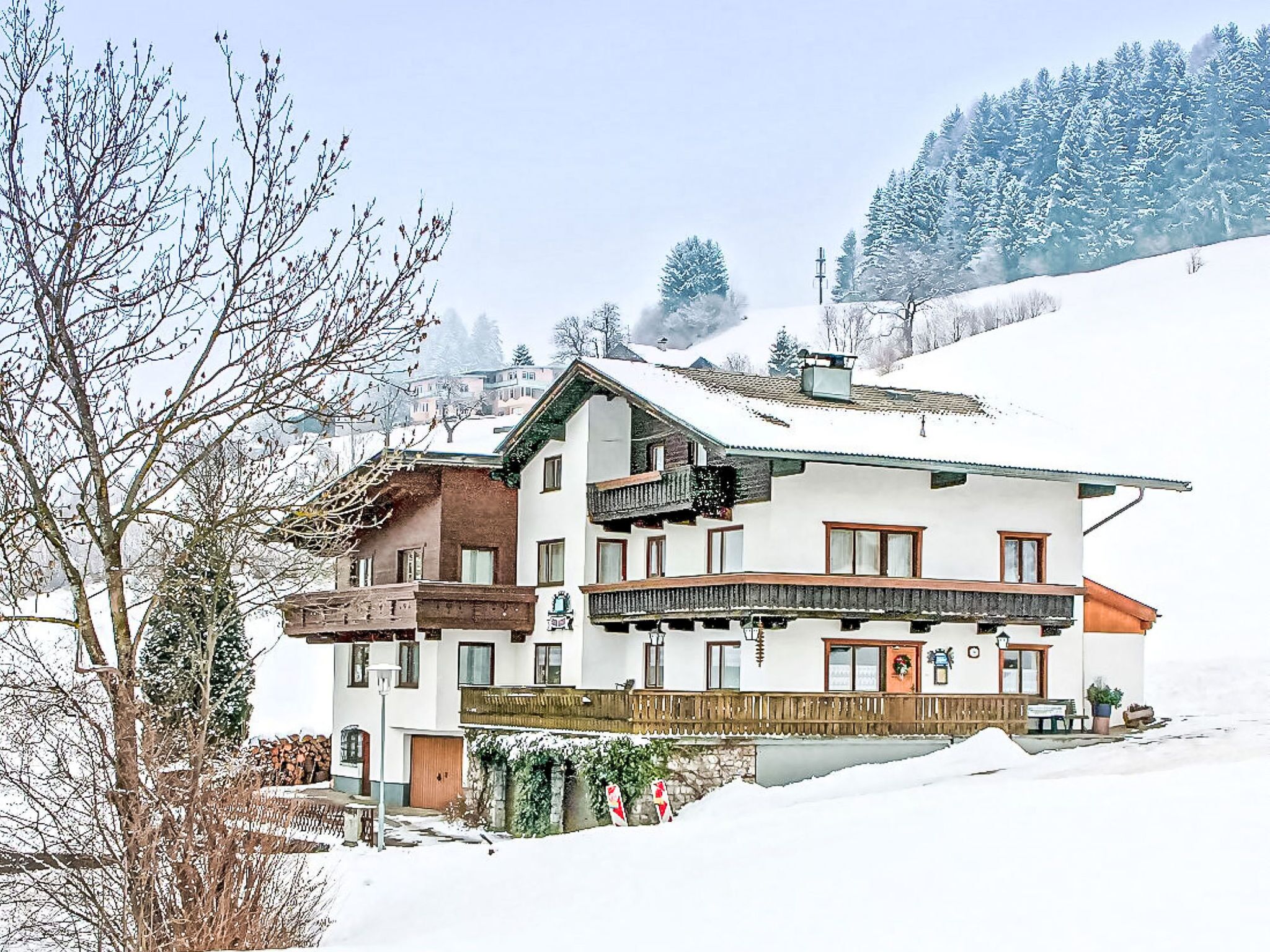 Un chalet à deux étages doté d’un balcon, entouré d’arbres couverts de neige et avec une chaîne de montagnes en toile de fond.