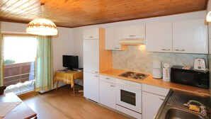 A compact kitchen with white cabinets, a stove, a sink, and a table with a television. - Jägerhof by Interhome (Schwaz)